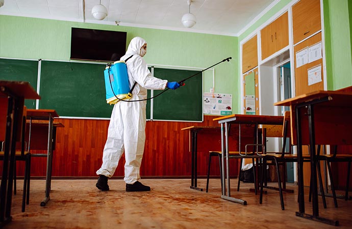 man sprays disinfection desks at the daycare center